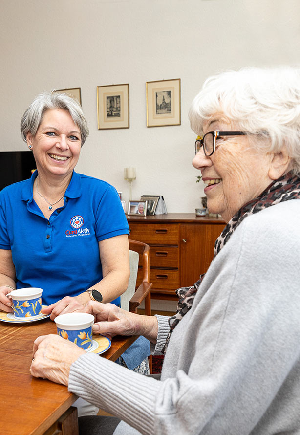 Pflegerin sitzt am Tisch mit Seniorin beim Kaffee trinken